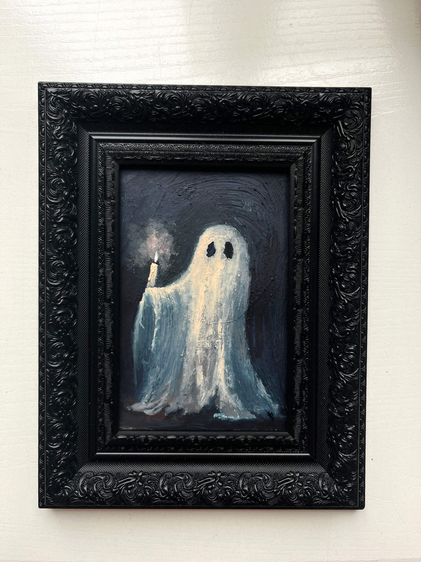 Framed artwork of a ghost holding a candle on a white wall