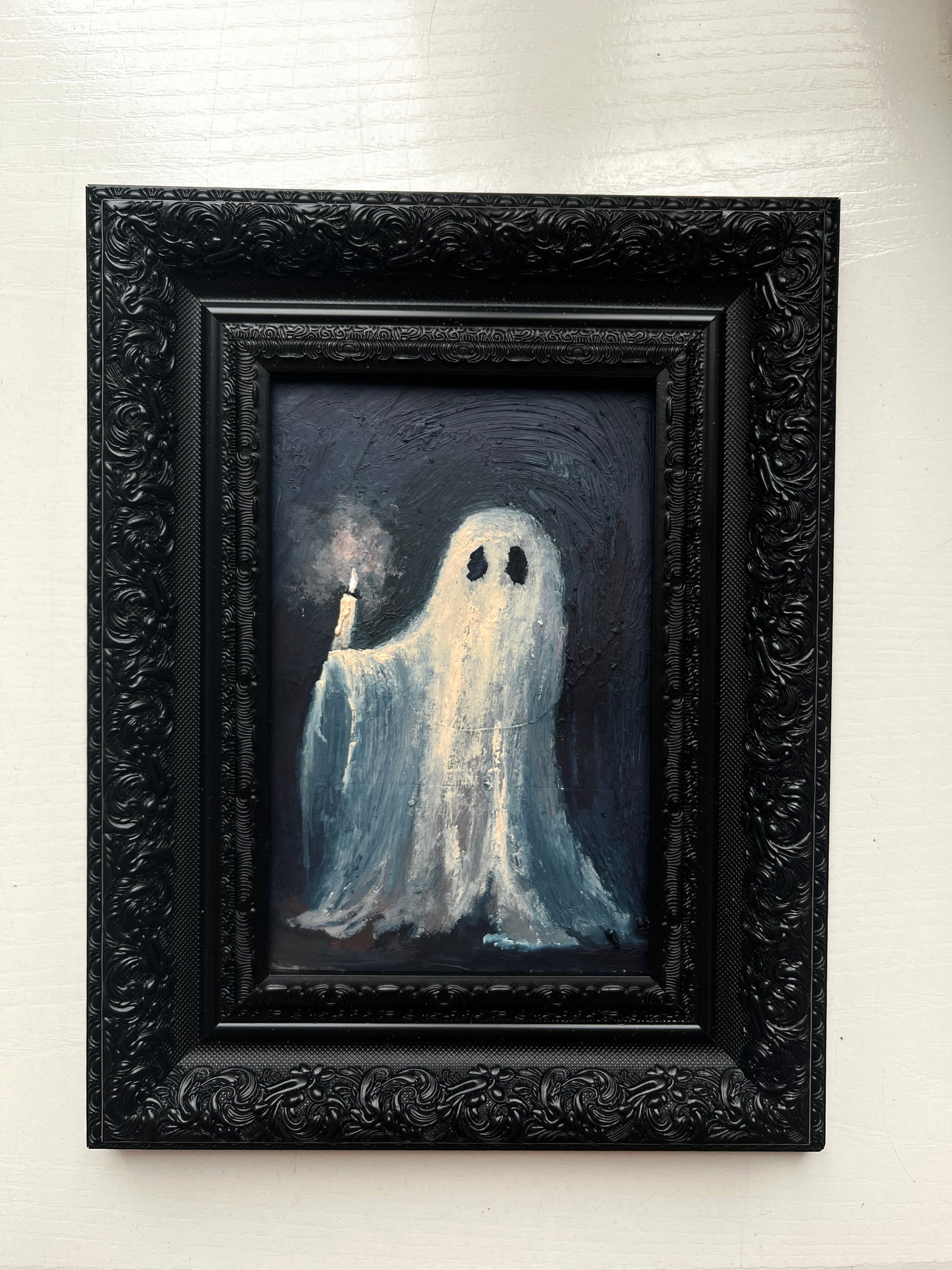 Framed artwork of a ghost holding a candle on a white wall