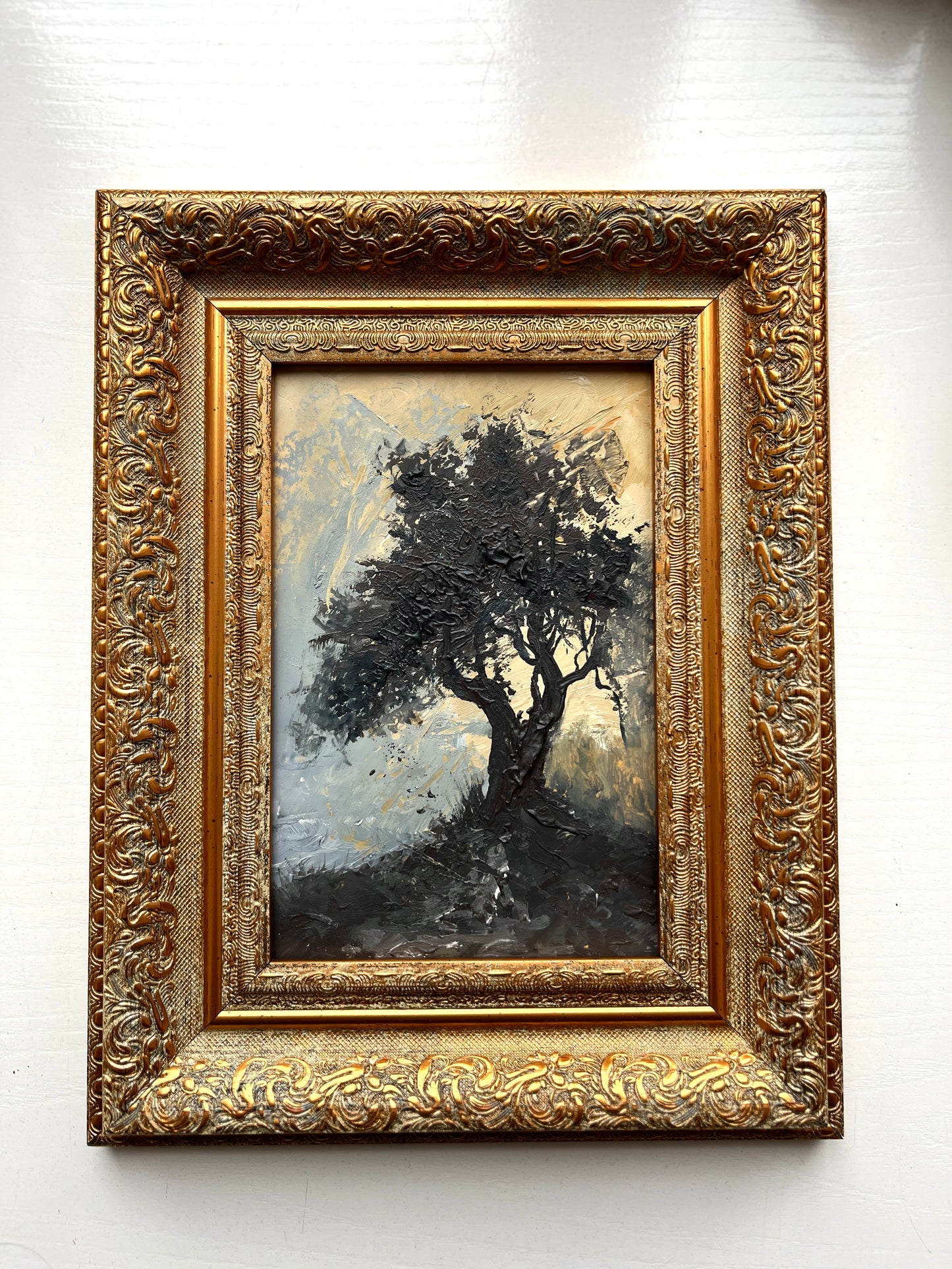 Framed painting of a tree with intricate gold frame on a white wall