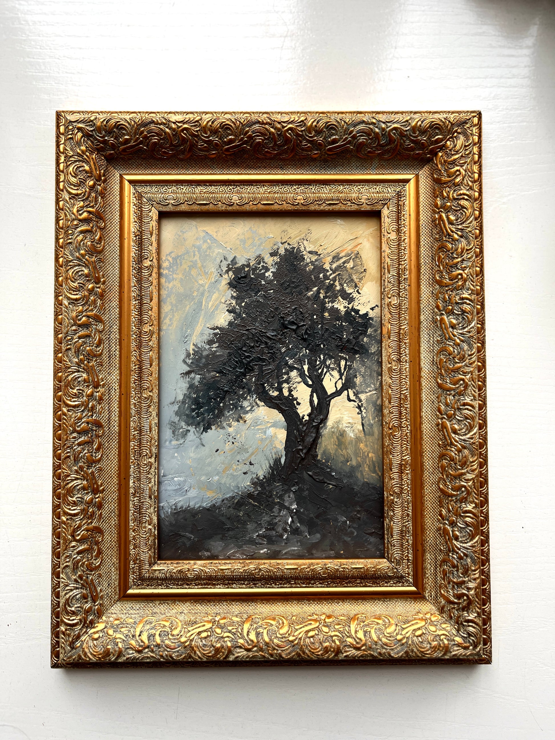 Framed painting of a tree with intricate gold frame on a white wall