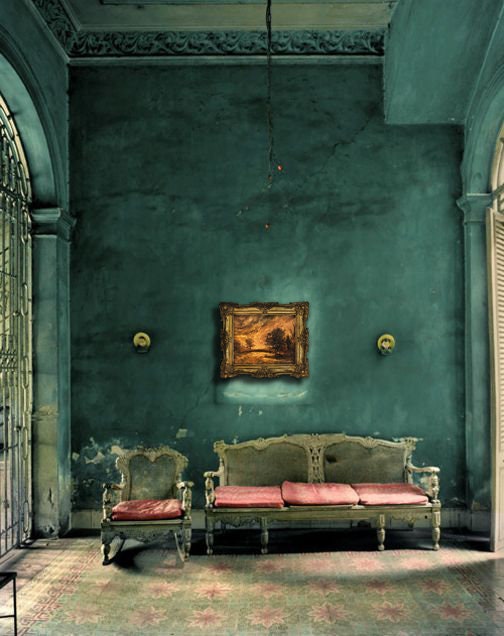 Vintage-style room with teal walls, a sofa, and chairs with red cushions.