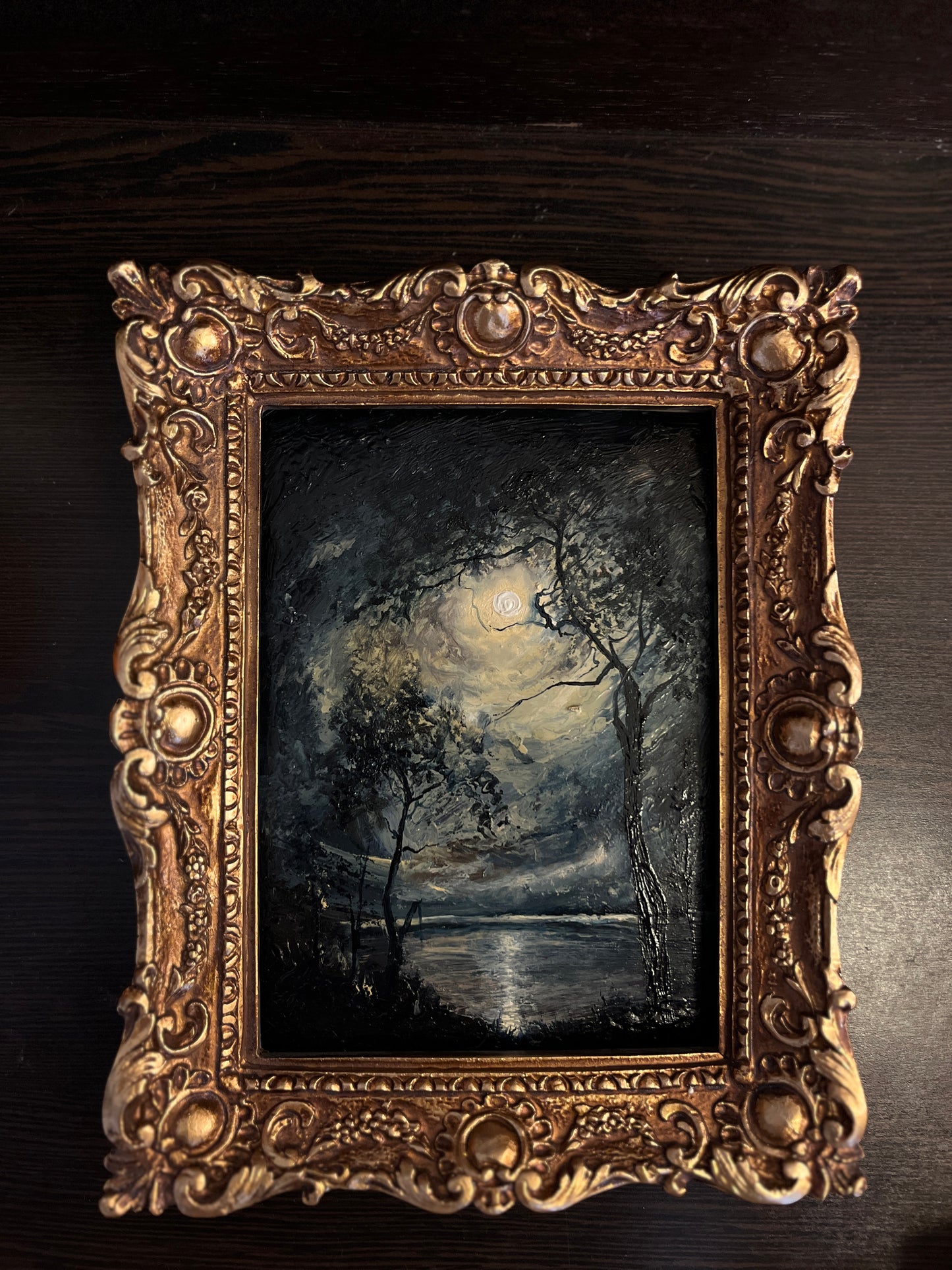 Small framed night landscape oil painting styled as dark academia decor on a wooden bookshelf