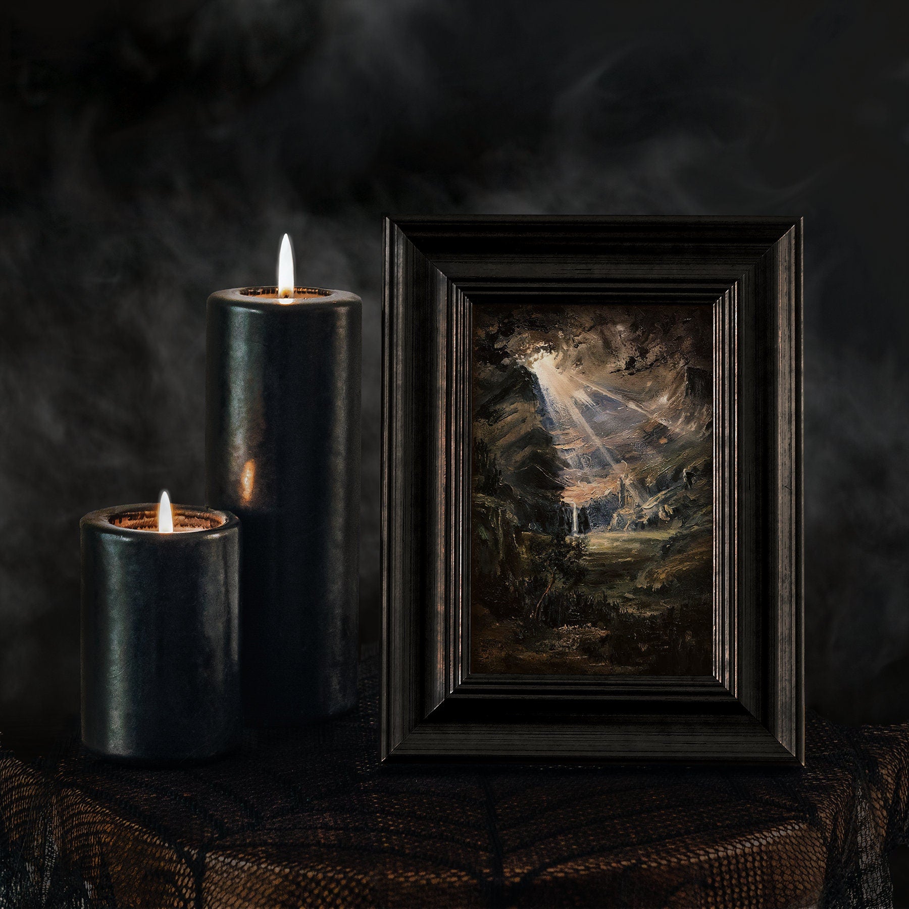 Framed artwork next to two black candles on a dark background
