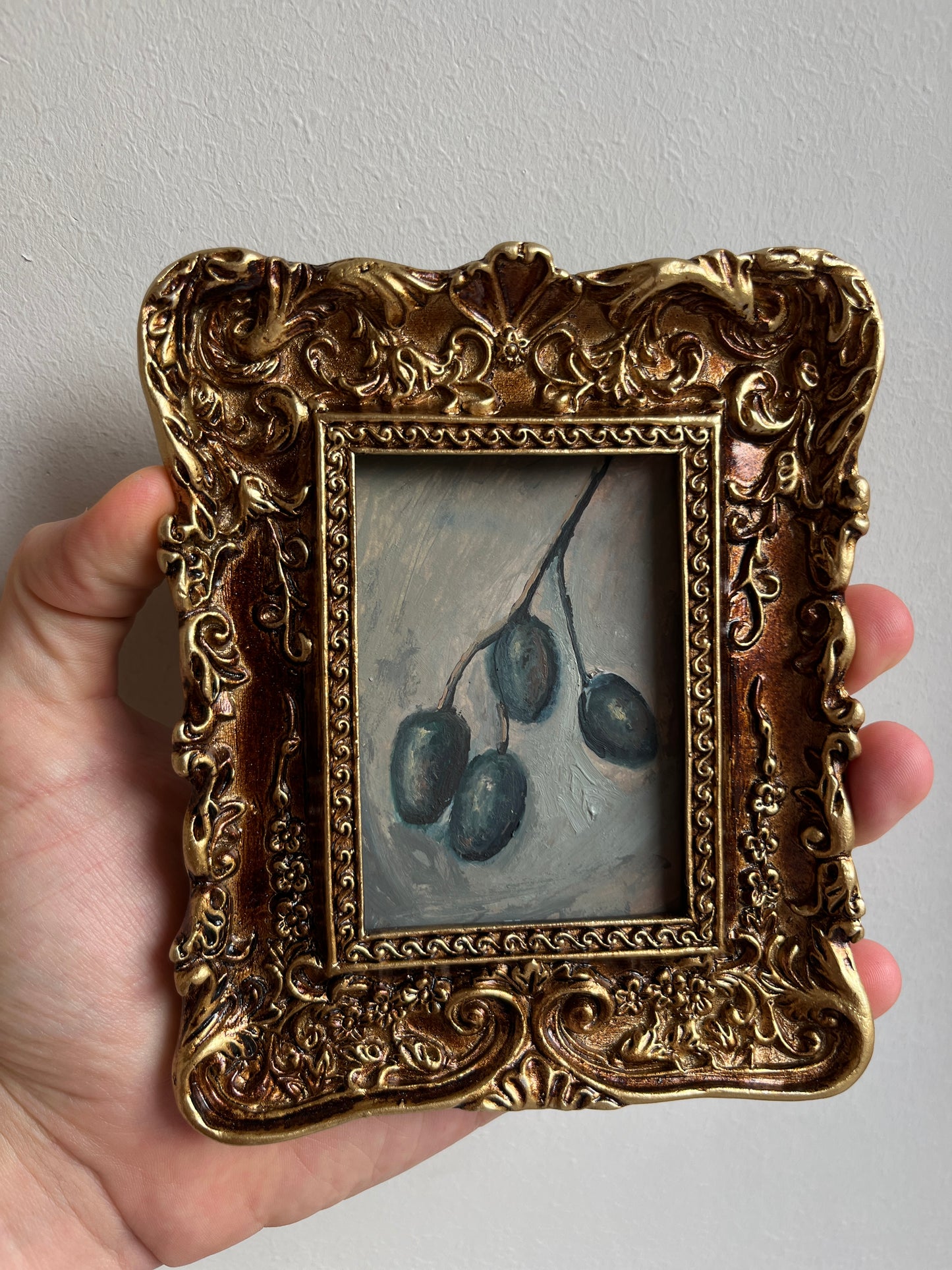 Small framed olive oil painting styled as elegant kitchen wall decor near a wine rack