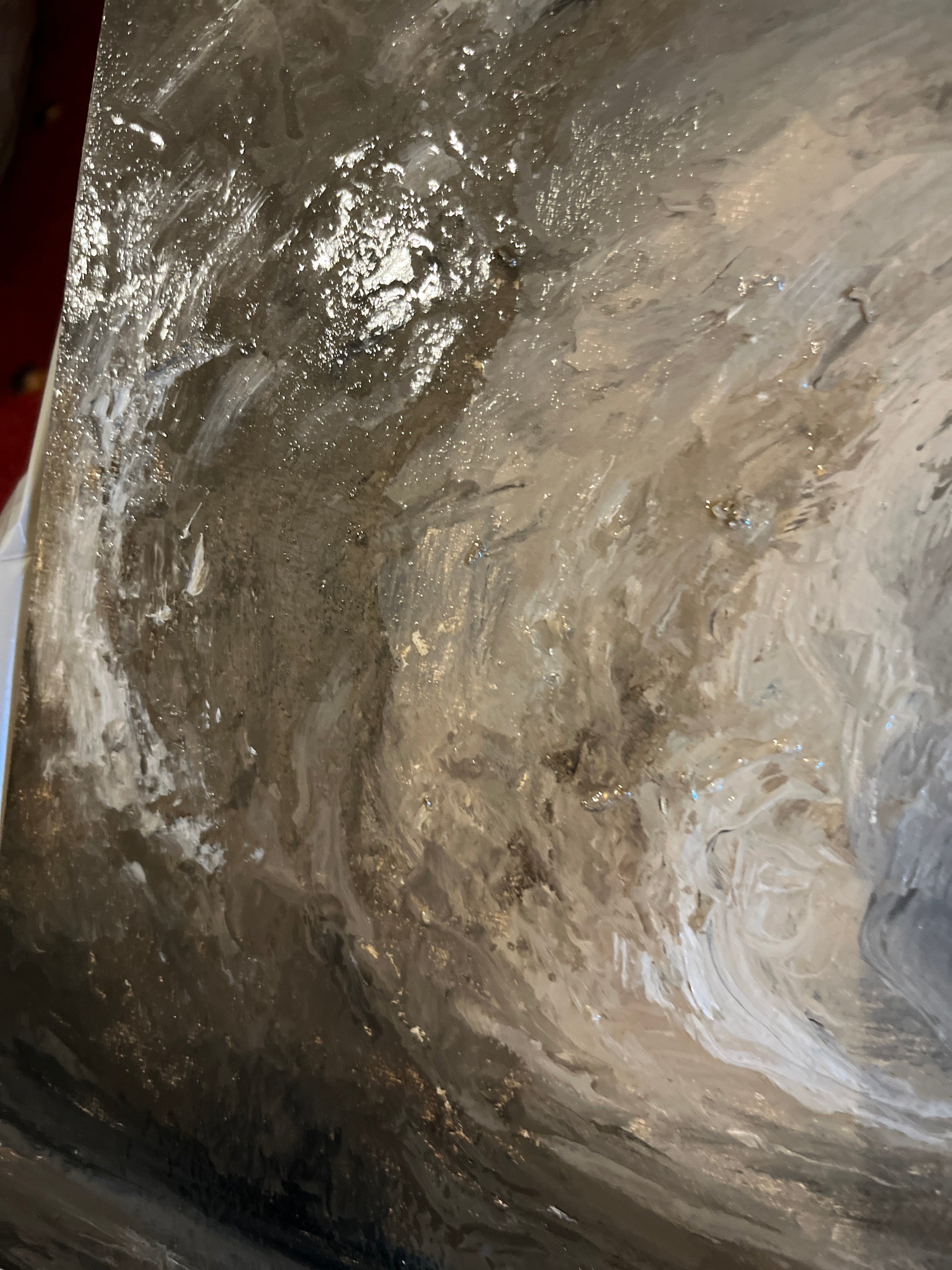 An abstract textured painting featuring swirling, fluid brushstrokes in shades of gray, white, and metallic silver with subtle gold flecks.